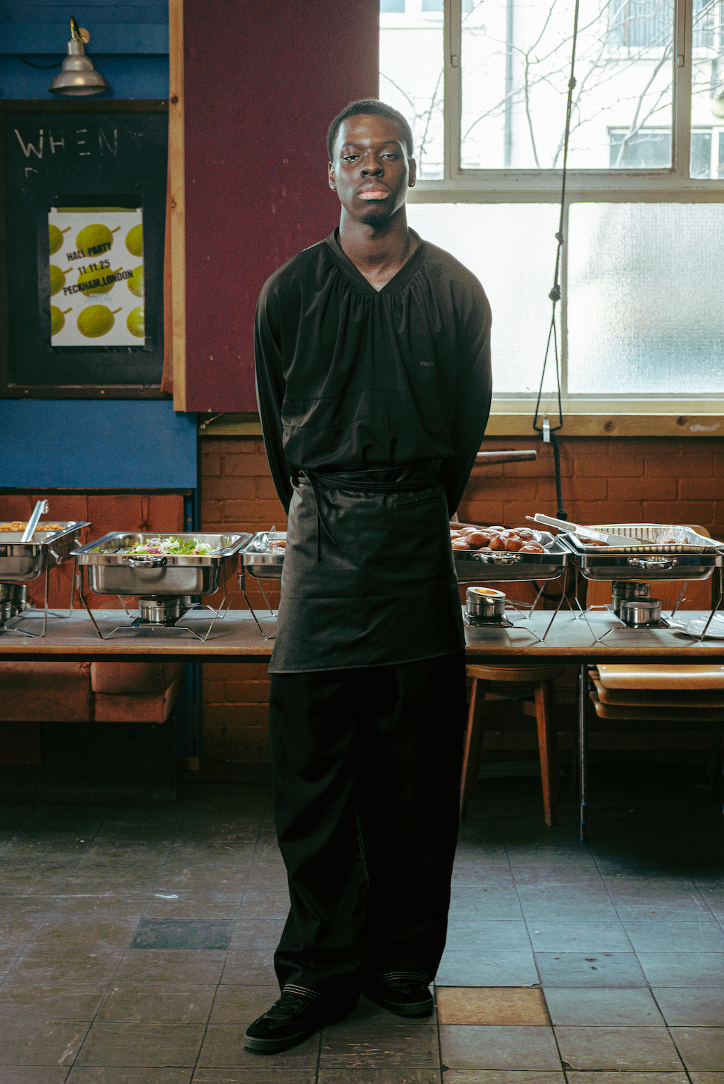 Person wearing a black apron standing in a kitchen with food preparation areas.